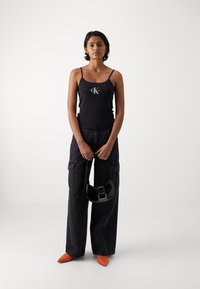 Black camisole with "CK" logo, paired with dark cargo pants, orange pointed-toe shoes, and a small black handbag. Simple design.