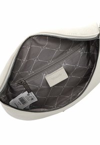 Intérieur d'un sac en cuir blanc avec un revêtement en tissu gris à motifs, comportant une poche zippée, une étiquette de marque et une fermeture éclair lisse.