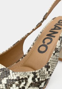 Γόβα με ψηλό τακούνι και λουράκι στο πίσω μέρος, με γυαλιστερό μοτίβο φιδιού σε μαύρο και λευκό, λεία υφή και μπεζ εσωτερικό με λογότυπο.