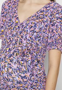 Těhotenský top s překříženým designem, barevným vzorem listí v růžové, fialové a žluté barvě, krátké rukávy a uvázaný detail v pase.