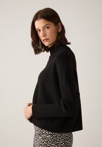 Schwarzer Strick-Turtleneck-Pullover mit gerippten Bündchen und Saum. Das Modell trägt einen gemusterten Rock, der eine lässige Passform und ein zeitgemäßes Design zeigt.