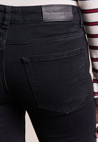 Svarta denimjeans med en smidig, figursydd design. Funktioner inkluderar en bakficka och en svart läderetikett med texten "The Kooples JEANS."