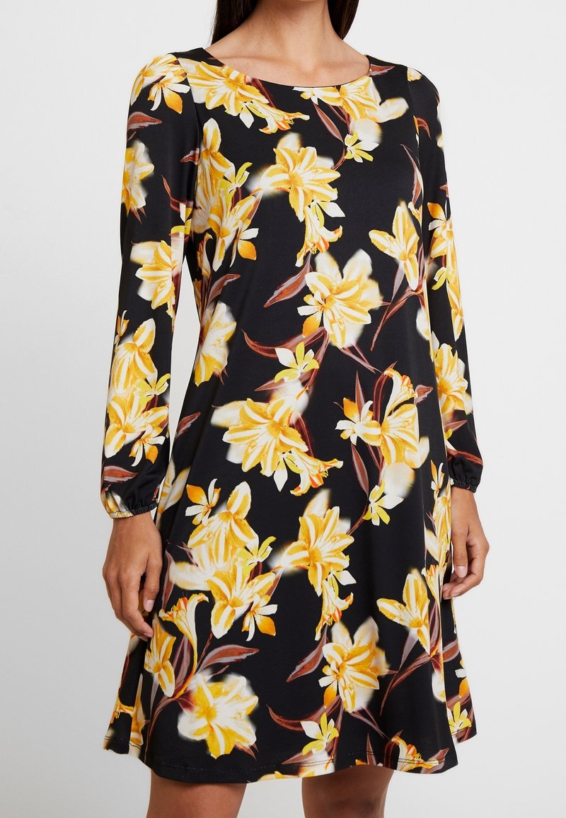 Vestido negro con patrón floral amarillo, mangas largas con puños elásticos y cuello redondo. Confeccionado en una tela suave y lisa.