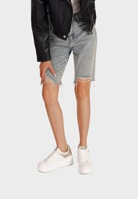 Shorts in denim chiaro con orli sfrangiati, abbinati a sneaker bianche con plateau dotate di accenti metallici e dettagli testurizzati.