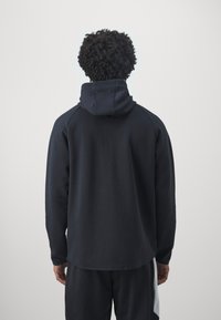 Navy hoodie with a kangaroo pocket, raglan sleeves, and adjustable drawstring. Soft fabric with a smooth texture, laid flat.