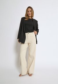 Crna blazerica preko uskog crnog topa, uparena s hlačama širokog kroja boje slonovače visokog struka. Svijetle sandale upotpunjuju outfit.