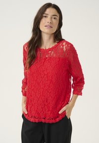 Haut en dentelle rouge avec un col en scallop et des manches trois-quarts. Présente un motif floral texturé et une coupe décontractée, ample.