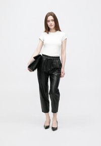 Zwarte broek van imitatieleren met een elastische tailleband, gecombineerd met een nauwsluitend wit T-shirt en zwarte pumps met een spits toeontwerp. Inclusief een zwarte clutch.