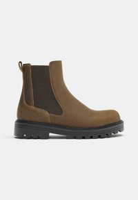 Botte Chelsea en daim marron avec panneaux élastiques sur les côtés, languette de tirage et semelle noire épaisse à crampons.