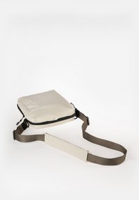 Beige schoudertas met een glad oppervlak, voorzien van een zwarte rits en een verstelbare bruine schouderband. Eenvoudige rechthoekige vorm, lichtgewicht ontwerp.