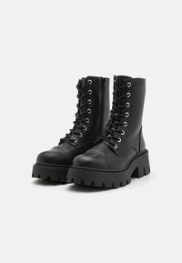Black leather ankle boots with a chunky sole, lace-up front, and side zipper. Features metal eyelets and a textured sole for grip.