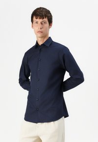 Camisa de manga larga azul marino con cuello abotonado, botones frontales y corte recto, hecha de una tela suave.