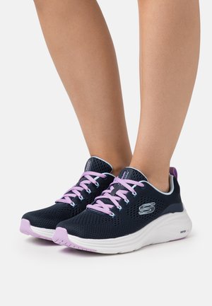 Scarpe da ginnastica in mesh nere con lacci e dettagli rosa. Suola bianca imbottita, punta arrotondata e logo sul lato.
