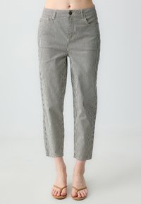 Pantaloni a righe in cotone bianco e nero con vestibilità slim, vita media, tasche frontali e orli cuffiati. Piedi con sandali marroni.