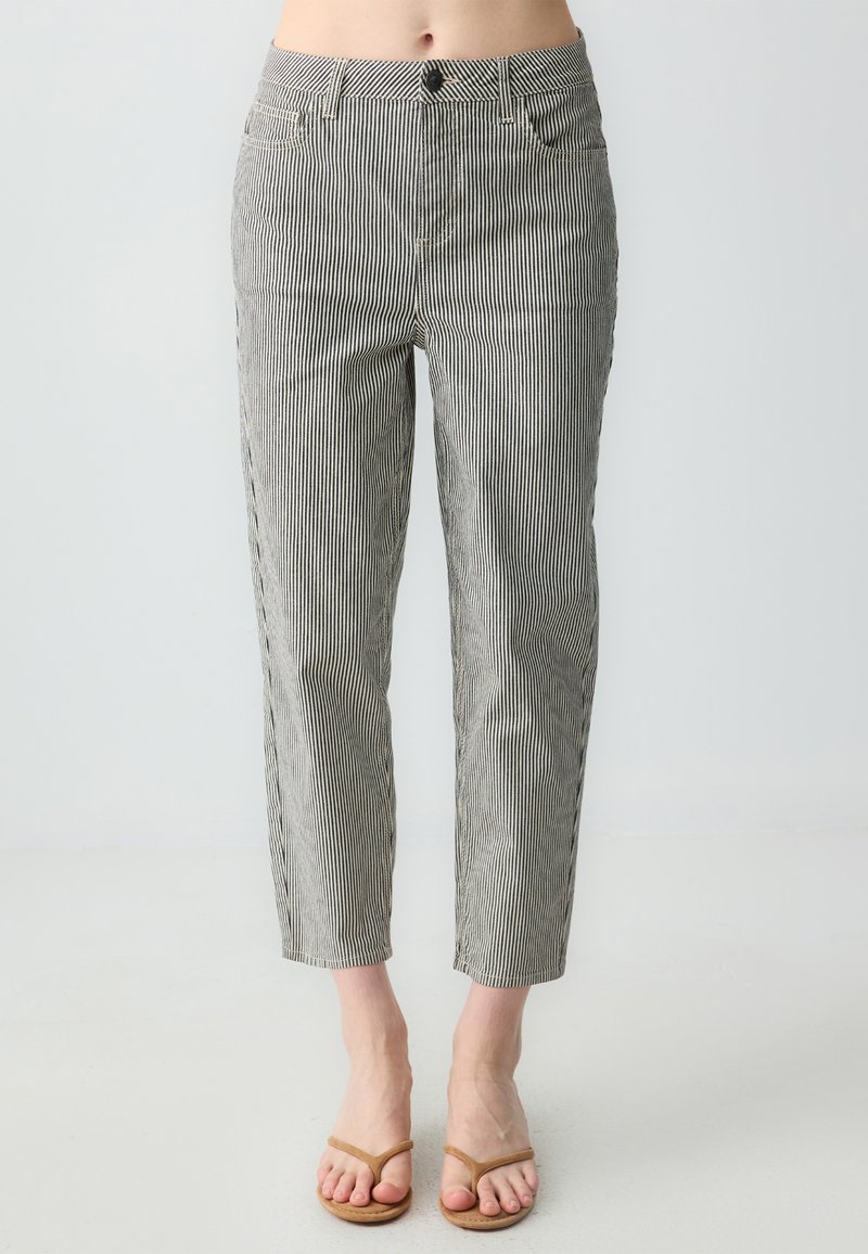 Pantalon rayé en coton noir et blanc avec une coupe slim, taille mi-haute, poches avant et ourlets retroussés. Pieds chaussés de sandales marron.