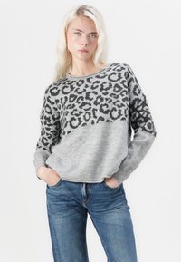 Pull en tricot gris avec un motif léopard noir sur la moitié supérieure. Manches longues et col rond avec des poignets côtelés.