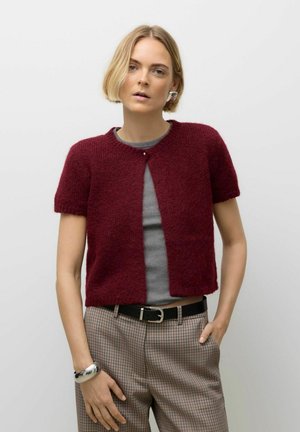 Cardigan en maille bourgogne à manches courtes avec une fermeture à boutons, associé à un haut gris et un pantalon à carreaux. Caractéristiques de design minimaliste.