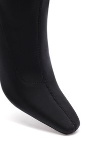 Botín negro de tobillo hecho de un material similar al cuero suave, con una punta afilada y costuras delineadas, que presenta una silueta ajustada y elegante.