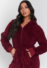 Sudadera de cremallera burdeos hecha de suave forro polar texturizado, con capucha, puños acanalados y dos bolsillos frontales, y presenta un patrón de diamantes.