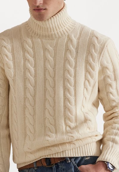 Kabelbrei turtleneck trui in crème. Gemaakt van dikke garen met verhoogde patronen, geribbelde kraag en zoom, en een gestructureerd ontwerp door het geheel.