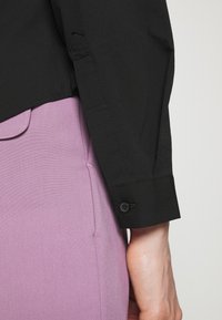 Zwarte lange mouwen shirt met een knopenmanchet, gecombineerd met een lichtpaarse broek. De stof lijkt glad met een subtiele glans.