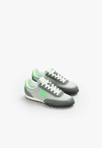 Graue und grüne Sportschuhe mit einem Obermaterial aus Wildleder und Stoff, weißen Schnürsenkeln und einer dicken schwarzen Gummisohle, die ein grünes Logo an der Seite haben.