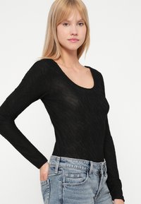 Haut noir à manches longues avec un design texturé semi-transparent, doté d'un col arrondi. Associé à un short en denim taille haute bleu clair.
