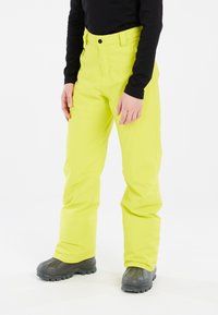 Fluorescerende gele skibroek met een aansluitend ontwerp, gemaakt van duurzaam materiaal. Heeft een ritszak en een knoopsluiting. Zwarte top en grijze laarzen.
