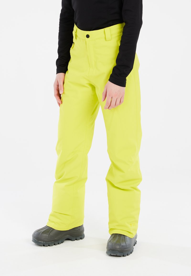 Fluorescerende gele skibroek met een aansluitend ontwerp, gemaakt van duurzaam materiaal. Heeft een ritszak en een knoopsluiting. Zwarte top en grijze laarzen.