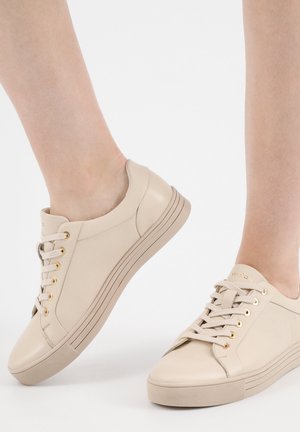Sneaker in pelle beige con punta arrotondata, occhielli dorati e lacci piatti. Presenta una superficie testurizzata e un design minimalista. Suola bassa.