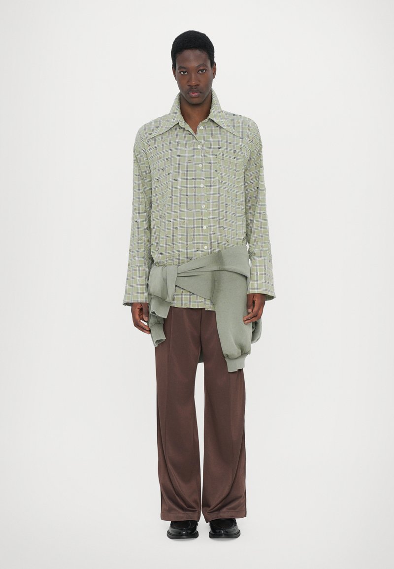 Green checkered long-sleeve shirt over a light green sweater, paired with brown wide-leg trousers and black shoes, worn by a person.