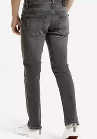 Wąskie szare dżinsy o gładkiej fakturze, z pięcioma kieszeniami i kontrastowym przeszyciem, połączone z białymi skórzanymi trampkami.