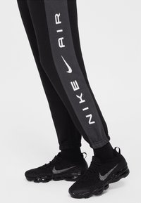 Black and gray athletic pants with white "Nike Air" branding along the leg, paired with black sneakers featuring a silver Swoosh logo.