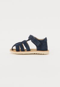 Sandalia de ante azul marino con punta y talón abiertos, que cuenta con múltiples correas y cierre de Velcro. Suela ligera y flexible con patrón en zigzag.