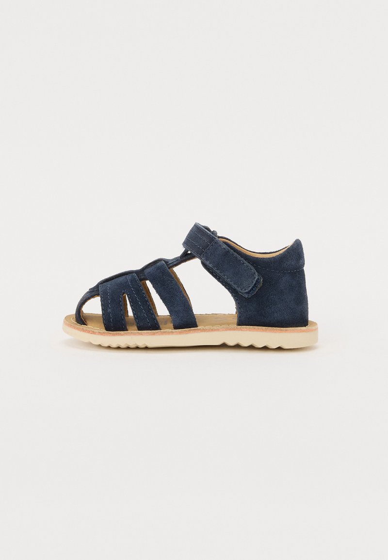 Sandalia de ante azul marino con punta y talón abiertos, que cuenta con múltiples correas y cierre de Velcro. Suela ligera y flexible con patrón en zigzag.