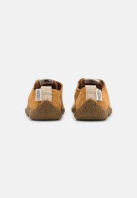 Scarpe slip-on in suede marrone con suola in gomma naturale testurizzata. Presentano un'etichetta in tessuto sulla linguetta e un piccolo logo sulla parte posteriore.