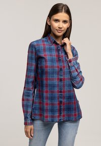 Niebiesko-czerwona koszula w kratę zapinana na guziki, z długimi rękawami i kołnierzykiem; posiada guziki z przodu oraz kieszeń po lewej stronie.