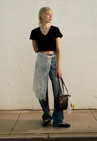 Haut noir en maille courte avec manches courtes, jeans bleu clair, châle floral transparent, et un sac à main noir avec un accent en dentelle et une étiquette colorée.