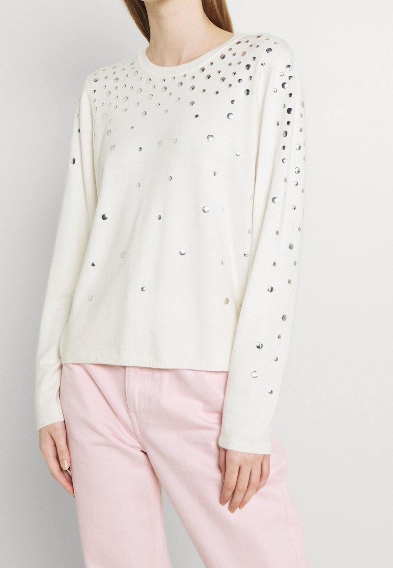 Cremfarbener Pullover mit silbernen Pailletten, die über die Vorderseite und die Ärmel verteilt sind. Mit Rundhalsausschnitt und gerippten Bündchen.