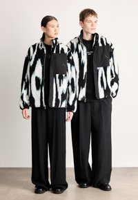 Fekete-fehér bolyhos dzsekik kék részletekkel, pattintós gombokkal, mellzsebekkel és laza szabással, fekete bő szárú nadrággal párosítva.