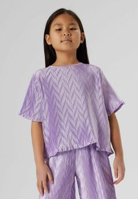 Violet krāsas īsām piedurknēm tops ar viļņainu tekstūru un brīvu piegriezumu; kombinēts ar atbilstošām violetām biksēm, abiem ar spīdīgu apdari un relaksētu dizainu.