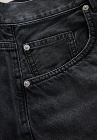 Gros plan sur un jean en denim noir montrant une poche avant avec des rivets métalliques et des coutures détaillées.