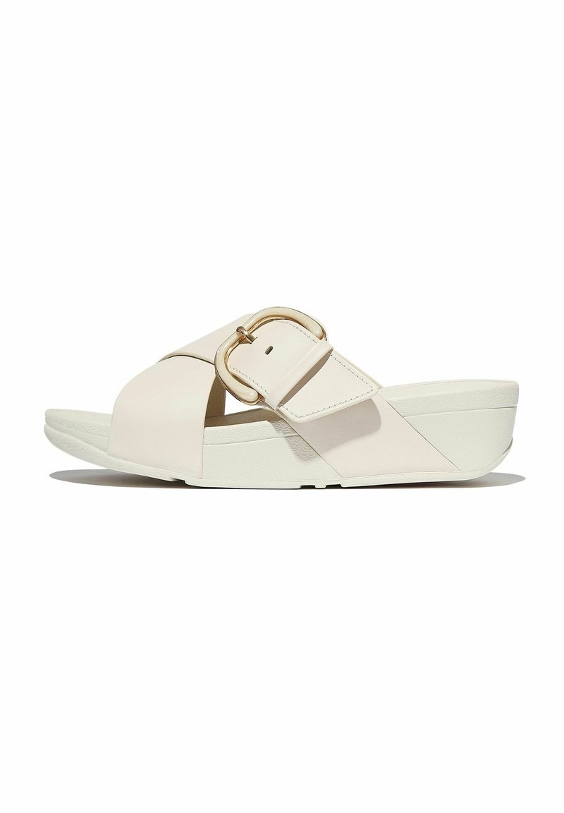 Sandale compensée beige à bout ouvert avec une large sangle traversant le pied et une grande boucle métallique sur le côté.