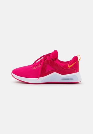 Zapatilla deportiva de color rosa brillante con suela blanca, logo Nike en naranja en el talón y cierre de cordones, mostrada de perfil sobre fondo blanco.