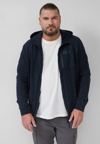 Marineblauwe zip-up hoodie met een kangoeroezak, een gestructureerd borstpaneel en een verstelbare trekkoordkap, gedragen over een wit T-shirt.