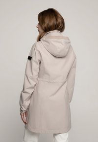 Beige waterdichte jas met een capuchon, verstelbare manchetten en een Taille met aansnoerpartij. Kenmerkend is de gladde textuur en een eenvoudig, gestroomlijnd ontwerp.