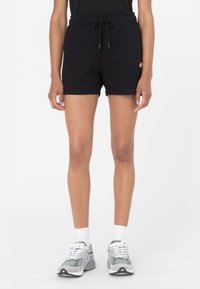 Pantalones cortos de algodón negros con banda elástica en la cintura y cordón. Presentan un pequeño logo en el muslo. Combinados con zapatillas de running grises y calcetines blancos.