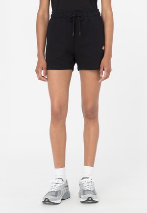 Pantalones cortos de algodón negros con banda elástica en la cintura y cordón. Presentan un pequeño logo en el muslo. Combinados con zapatillas de running grises y calcetines blancos.
