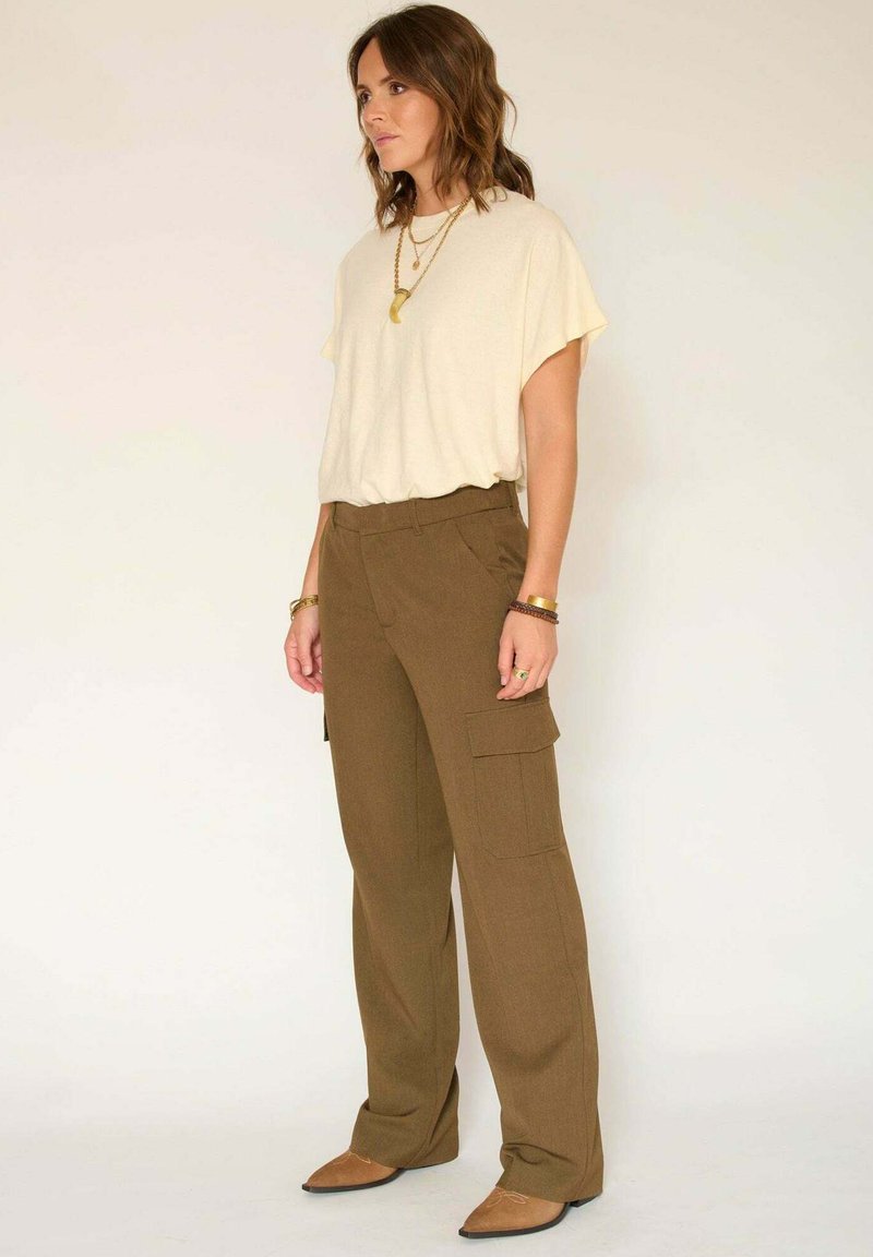 Haut beige à manches courtes associé à un pantalon cargo vert olive avec des poches latérales. Des ballerines marron à bout pointu complètent la tenue.