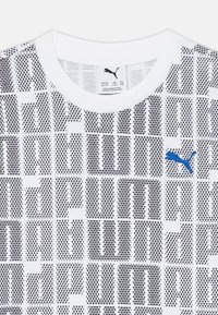 Camiseta blanca con patrones geométricos negros, que presenta un logo de Puma azul en el pecho y un escote redondo. Fabricada con tela suave.